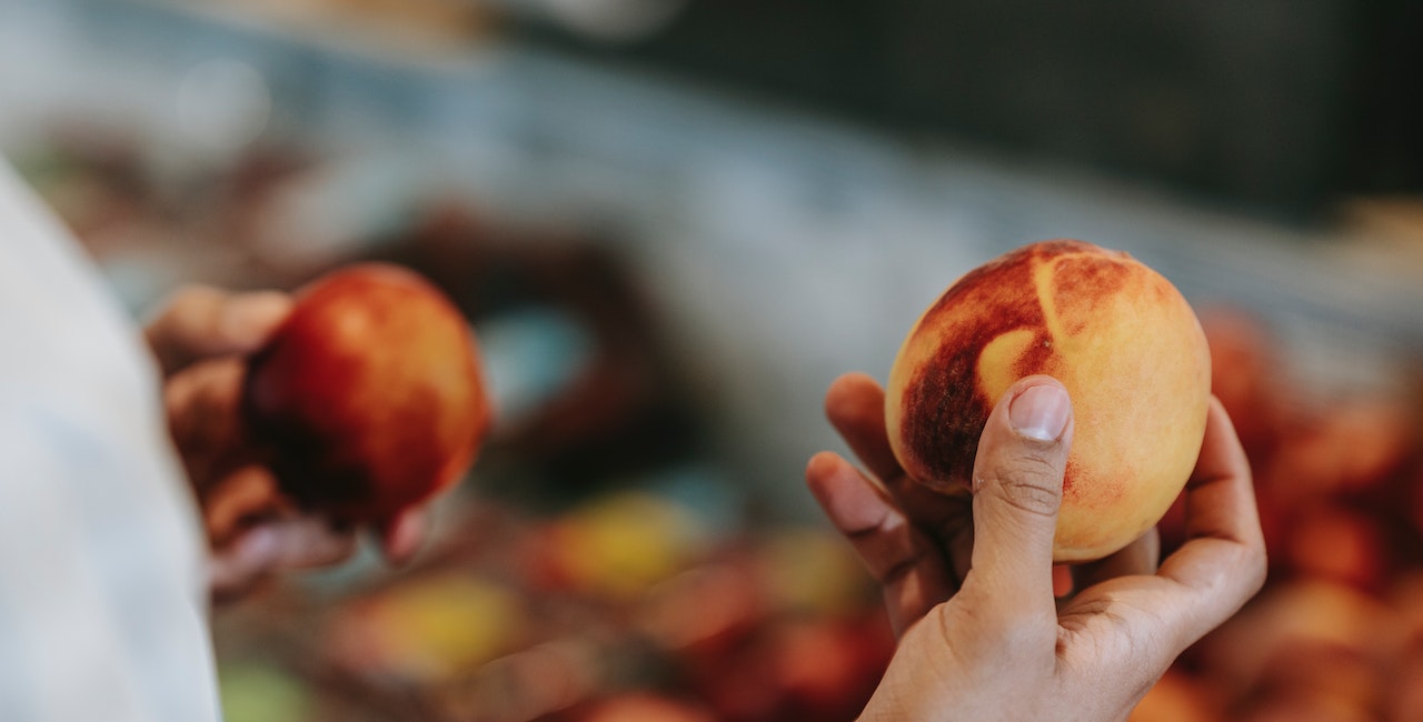 Photo of a person comparing peaches in a food market.